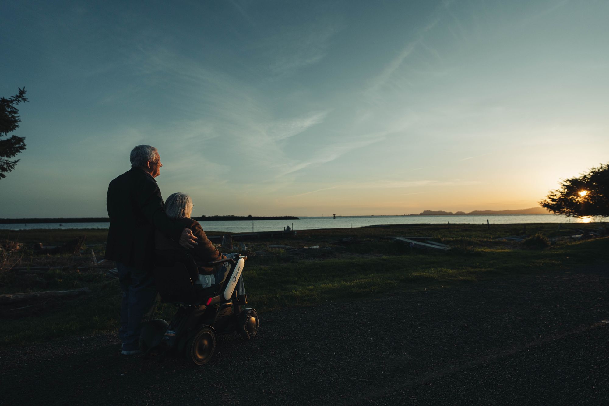 A wheelchair user with her husband watching the beautiful sunset over the ocean.