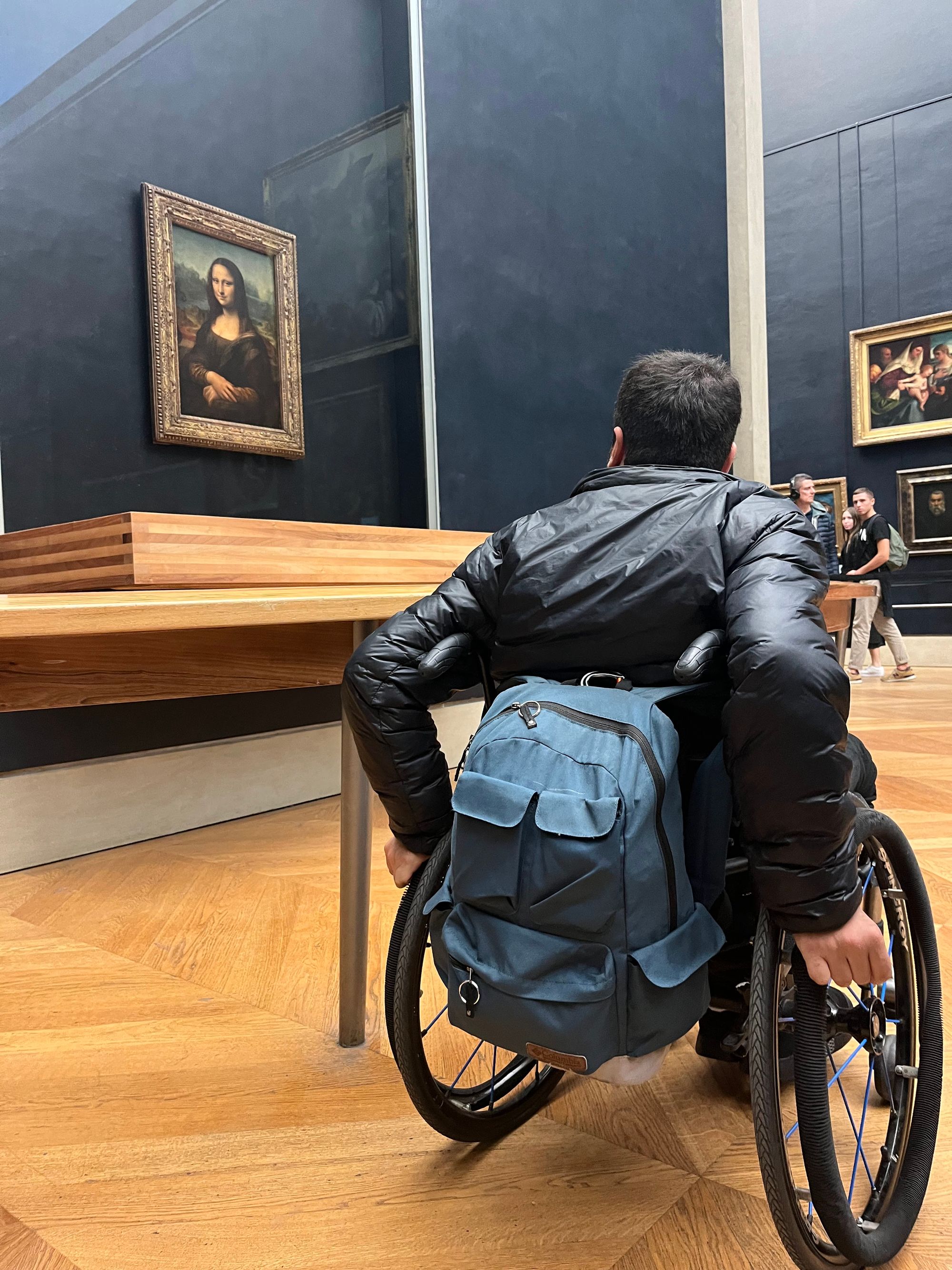 A wheelchair user at the Louvre museum observing the Mona Lisa painting.