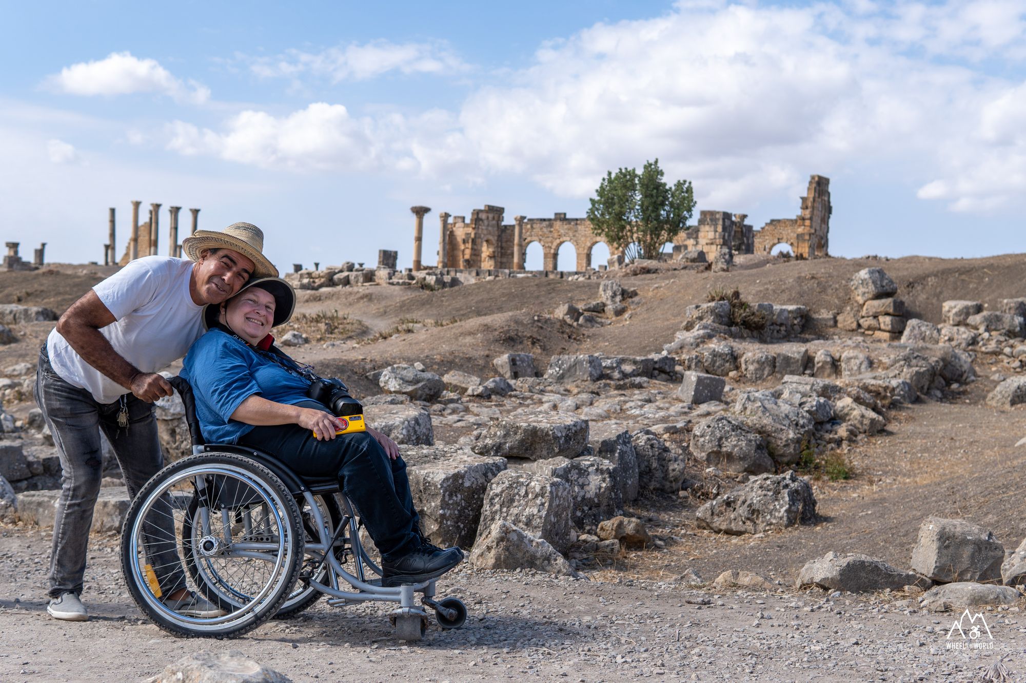 A wheelchair user being helped through the gravel trail in Morocco. A good representation of celebrating disability pride month.