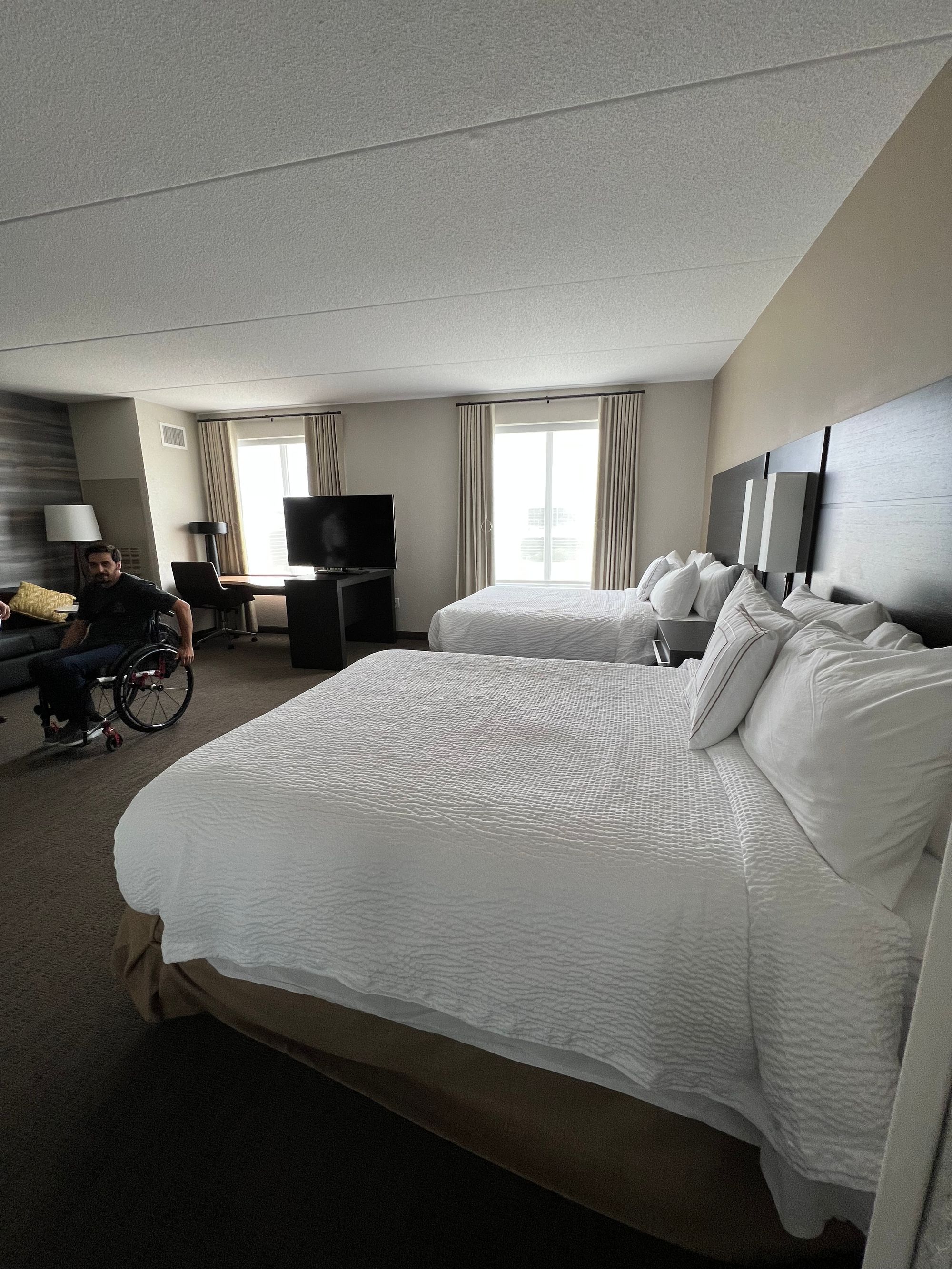 An accessible hotel room with a wheelchair user, showing ample space at the foot of the bed and between the beds