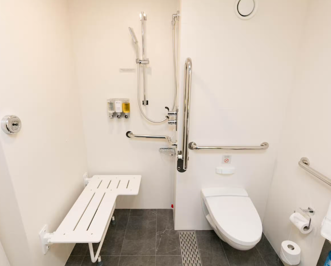 Roll-in shower with a shower seat, grab bars, and a toilet with grab bars