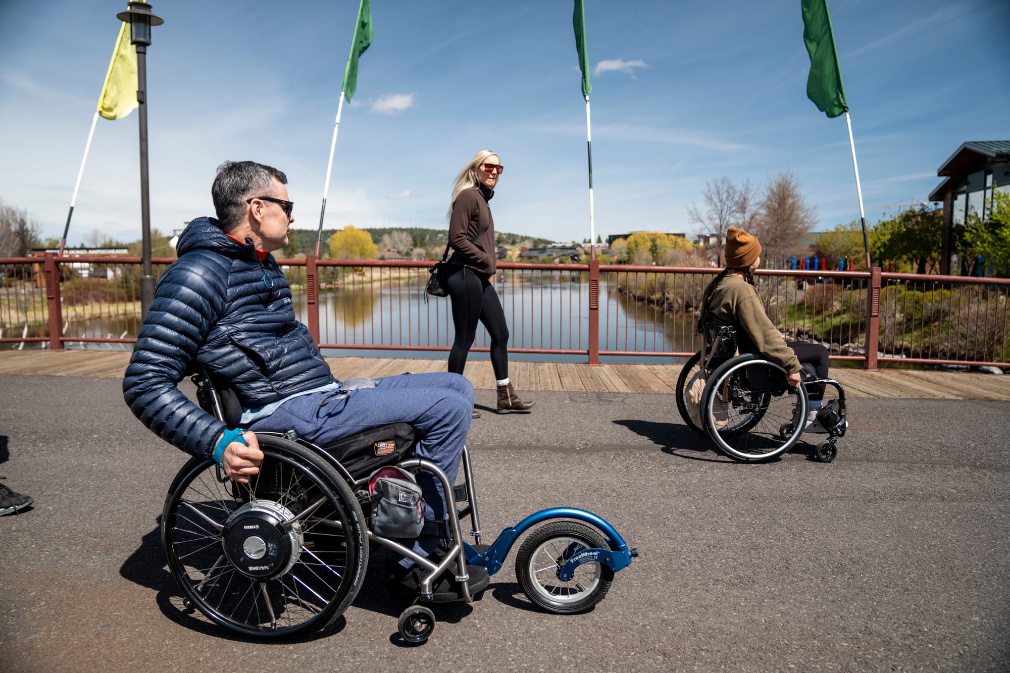 Two wheelchair-users exploring accessible pathways over the river in Central Oregon