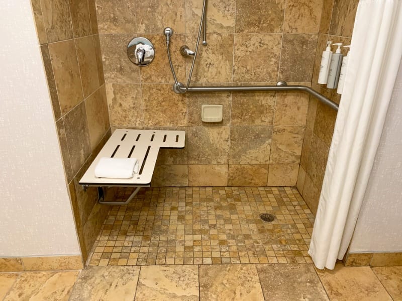 Roll-in shower with a shower seat and grab bars at Hampton Inn New Smyrna Beach