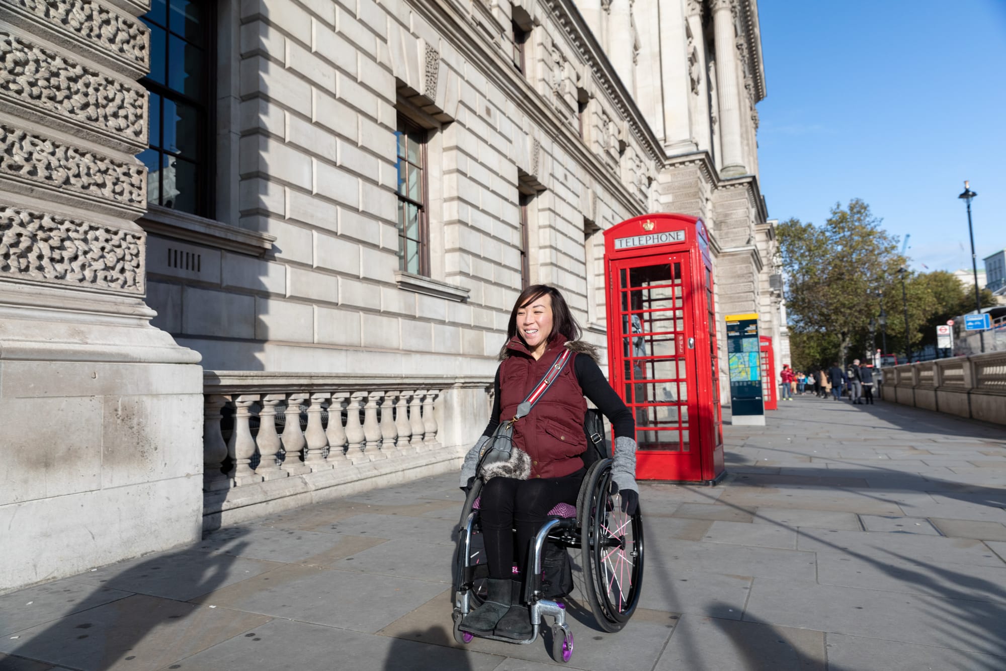 Wheelchair-user rolling down London sidewalks with red phone booth in background