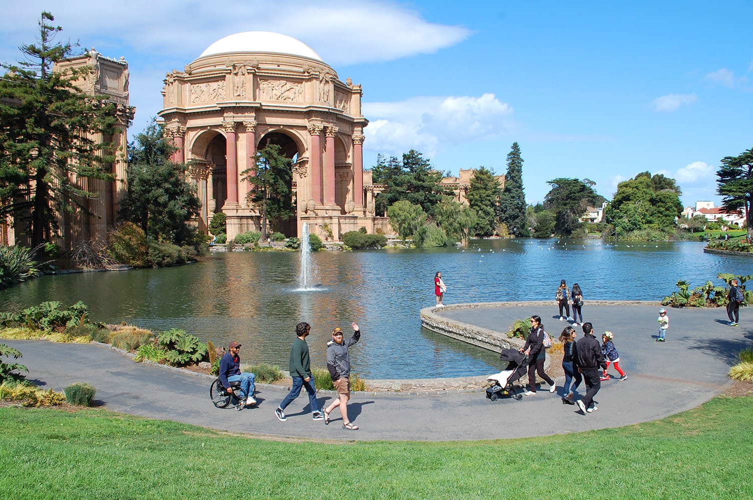 Wheelchair-user and friends on an accessible path in the Marina District of San Francisco. Palace of Fine Arts in the background