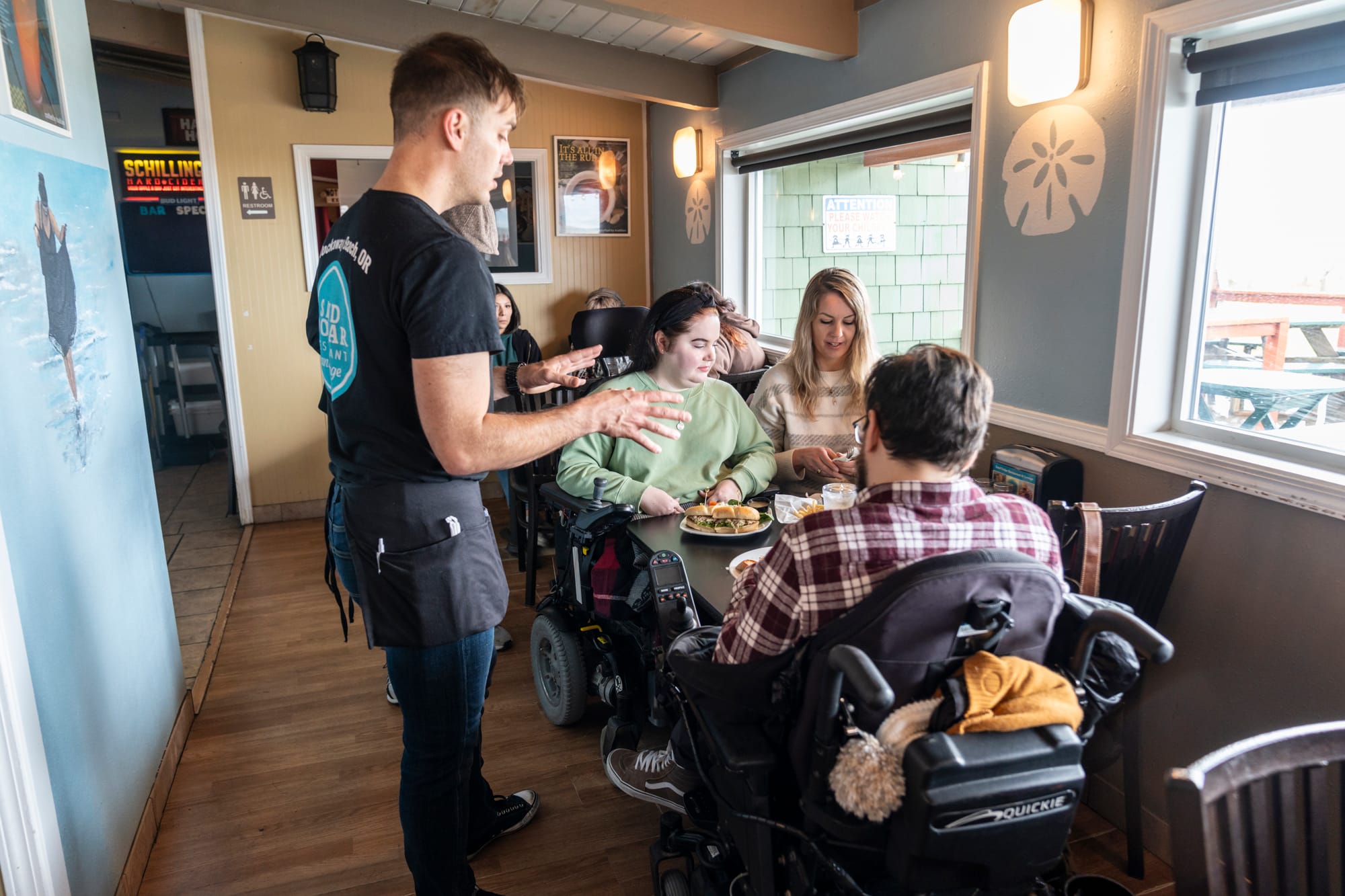 Local server helping two wheelchair users at an accessible restaurant in Tillamook Coast