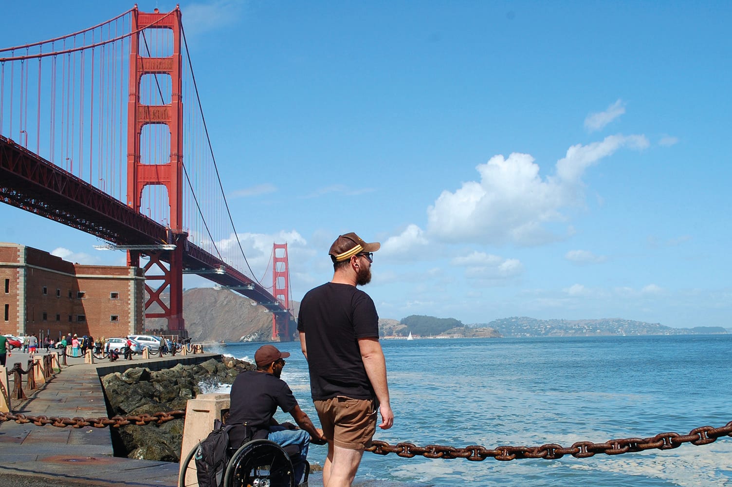 Wheelchair-user and companion enjoying ocean views in San Francisco with Golden Gate Bridge in the background