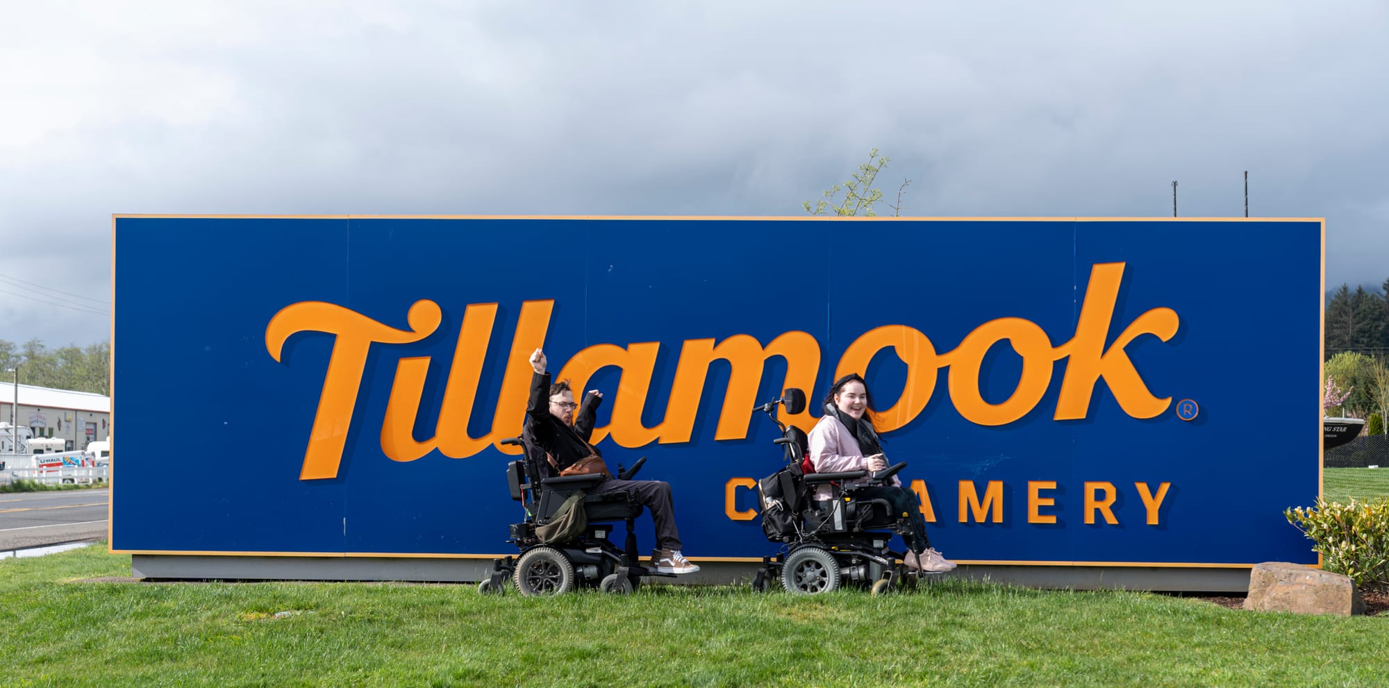 Two wheelchair-users in front of the Tillamook Creamery sign in Tillamook Coast, Oregon