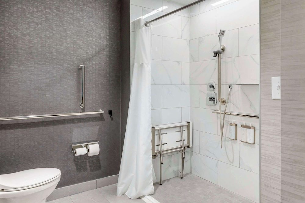Roll-in shower with a seat and grab bars at Cambria Hotel
