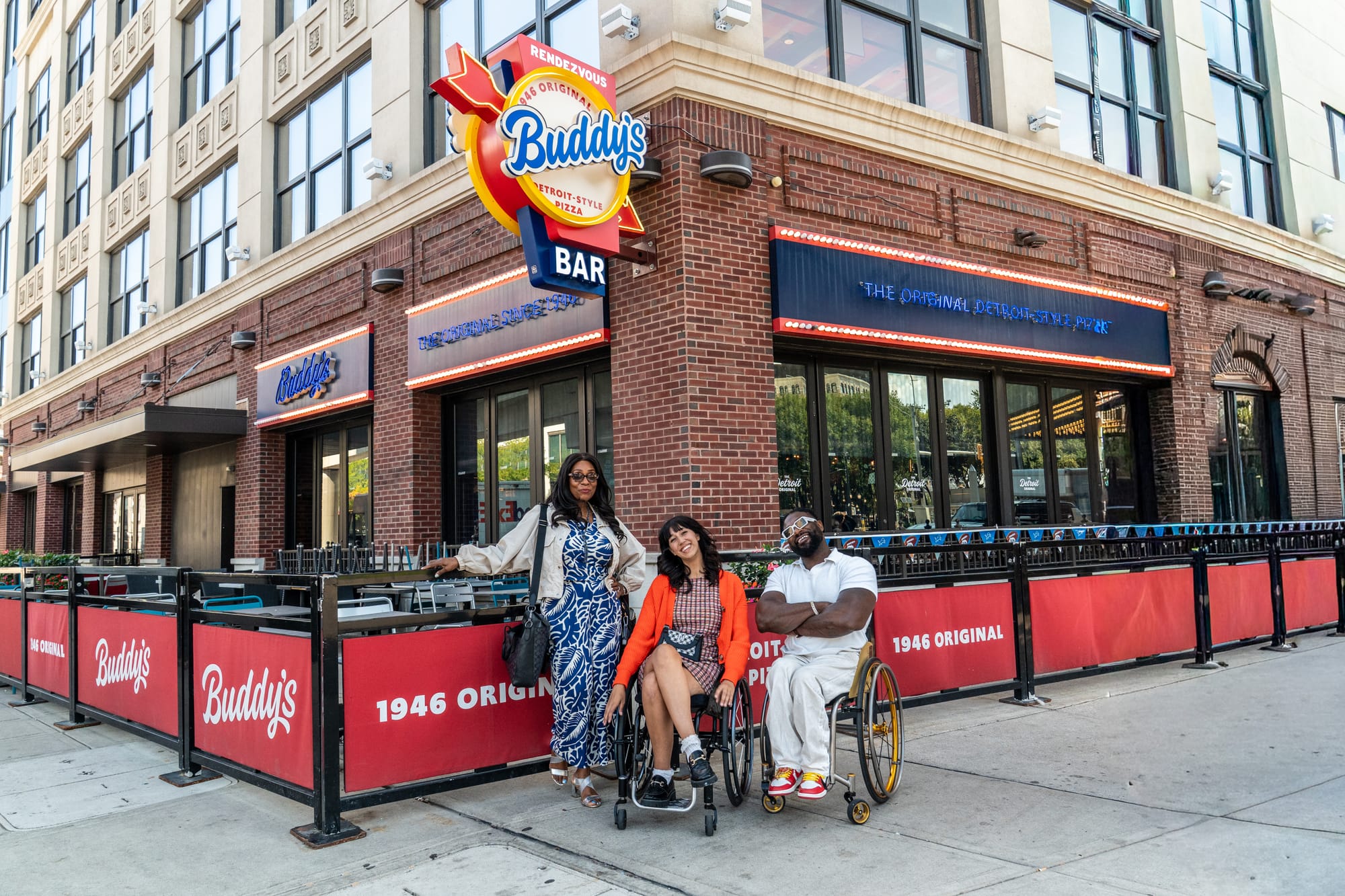 Two wheelchair users and companion in front of Buddy's Pizza