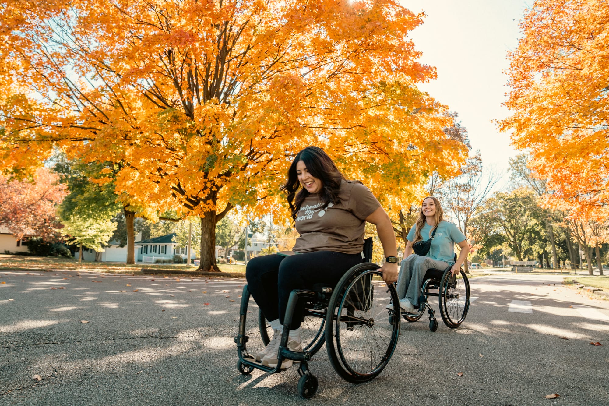 Erika and Stef, two wheelchair users, traveling in Grand Rapids with autumn trees in background