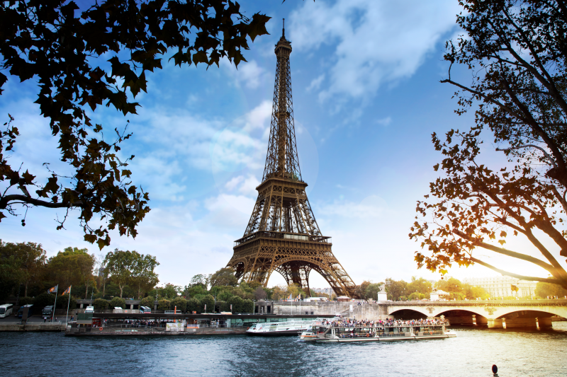 A beautiful view of the Eiffel Tower from across the Seine River, with a river cruise boat floating by.