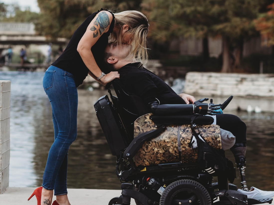 Triple amputee, Ryan Davis, kissing his wife while in a wheelchair