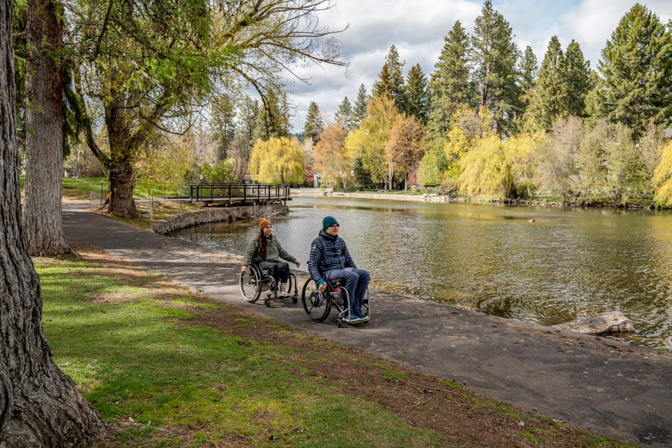 Two wheelchair-users rolling on accessible pathway around a pond in Central Oregon