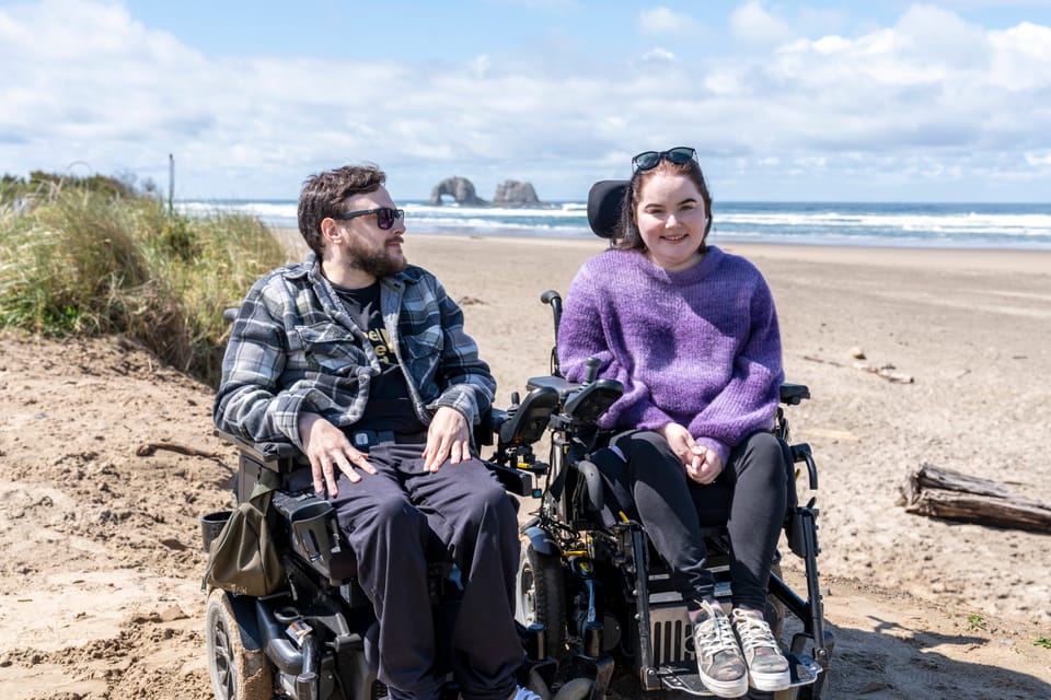 Two wheelchair users at Rockaway Beach, Tillamook Coast with ocean in the background