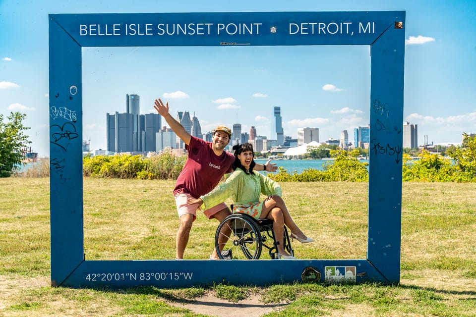 Wheelchair user and companion having fun at the Belle Isle Sunset Point sign in Detroit