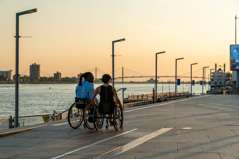 Two wheelchair users strolling down the Detroit Riverwalk during sunset