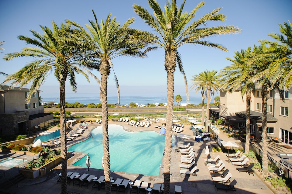 View overlooking pool with palm trees and beach at Cape Rey Carlsbad Beach hotel